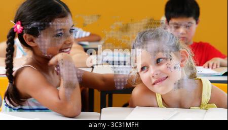 Smiling two girls leaning together and conversing in school classroom, with notebooks and pencils Stock Photo
