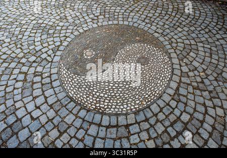 Overhead close-up of a decorative yin-yang pebble mosaic medallion set into cobblestone pavement in the Chinese Garden in Stuttgart, Germany. Stock Photo
