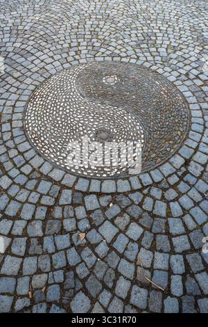 Overhead close-up of a decorative yin-yang pebble mosaic medallion set into cobblestone pavement in the Chinese Garden in Stuttgart, Germany. Stock Photo