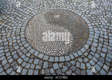 Overhead close-up of a decorative yin-yang pebble mosaic medallion set into cobblestone pavement in the Chinese Garden in Stuttgart, Germany. Stock Photo