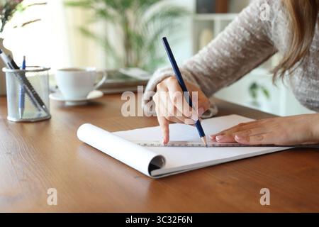 Close up of a woman hand using ruler to draw on notebook on a wooden table at home Stock Photo