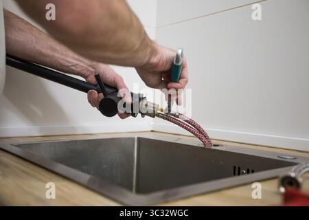 Professional plumber fixing water tap in kitchen, closeup Stock Photo