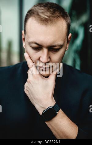 Man thinking with hand on chin in urban setting Stock Photo
