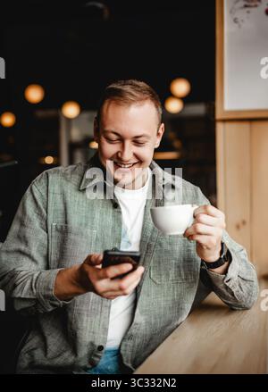 Smiling man using smartphone while drinking coffee Stock Photo
