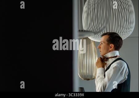 Man adjusting bowtie in modern interior with stylish lighting Stock Photo