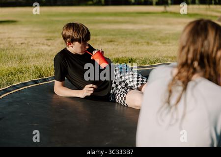 Teen boy lying on trampoline drinking with straw in backyard Stock Photo