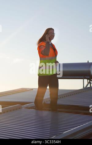 renewable energies. female solar panel installer technician checking an installation while talking on her cell phone. Stock Photo