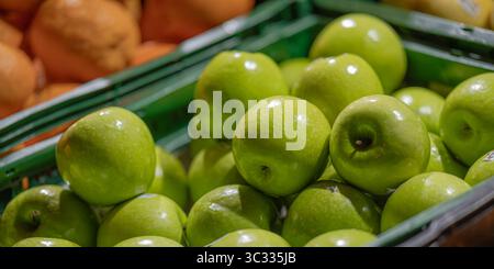 Close-up image of green apples in a plastic crate at a grocery store or market. The apples are glossy and fresh, with a slightly blurred background. Stock Photo