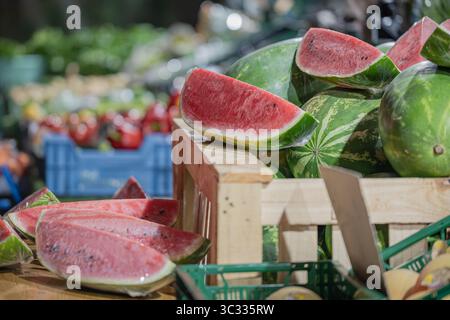 Close-up of sliced red watermelons arranged on a wooden crate at an outdoor street market. The vibrant fruit is wrapped in transparent plastic. Stock Photo