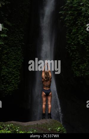Woman practicing yoga pose in front of majestic waterfall in jungle Stock Photo