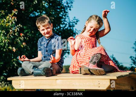 Boy meditating while girl is dancing on a wooden table in a garden Stock Photo
