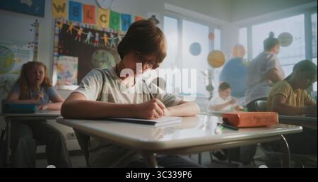 Concentrated Primary School Children Writing School Test on Geography or Ecology in Modern Classroom. Female Teacher Walking Between Desks, Controlling Group of Diverse Kids During the Exam Process. Stock Photo