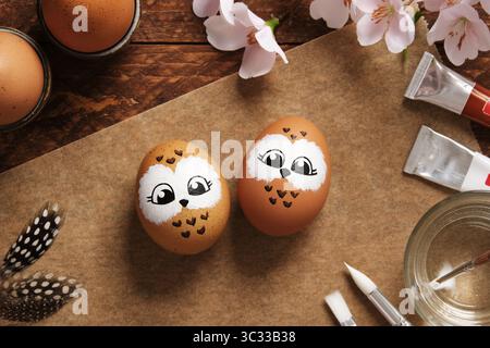 Easter eggs with owls, hand-painted with acrylic paints, on a background of paints, brushes, and palette. DIY concept Stock Photo