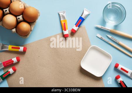 Easter egg decoration and creative preparation. A cardboard sheet on a blue background with brown eggs, brushes, and paint tubes. Stock Photo