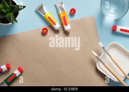 Preparing to draw. Tubes of acrylic paint, brushes, a glass of water on blue background. Place for your text. Stock Photo
