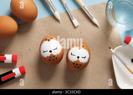 Easter eggs with sleeping owls, hand-painted with acrylics, on a background of paints, brushes and palettes. DIY concept Stock Photo