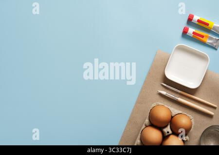 Easter egg decoration and creative preparation. A cardboard sheet on a blue background with brown eggs, brushes, and paint tubes. Stock Photo