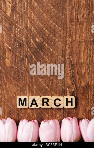 Word March in English made of wooden blocks with pink tulips on a brown wooden background. Space for your text. Stock Photo