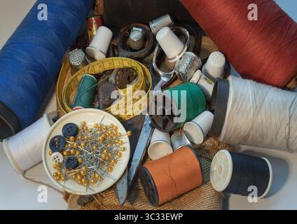 Sewing needles stuck in a green miniature spools thread Steel scissors, Spools of thread of various colour, Thimbles and Measuring tape including Pins Stock Photo