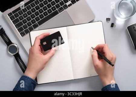 Work desk with computer, notepad, writing supplies. In one hand a man holds a bank card, in the other a pen. A place for your text. Stock Photo