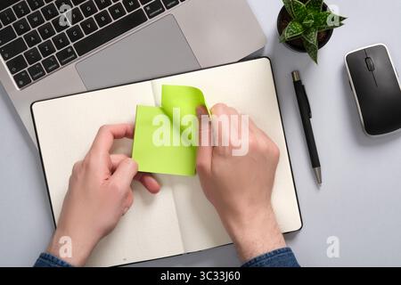 Hands peel off a green-colored sticker over an open notepad on a desk. A place for your text Stock Photo