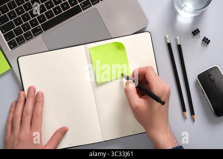 Hand writing on a green colored sticky note above an open notepad on a desk. opyspace Stock Photo