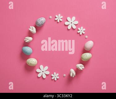 Minimalist Easter frame with white bunnies, colored eggs and wooden flowers on pink background. Space for your text. Stock Photo
