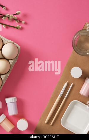 Preparing for the celebration of Easter. Gouache for painting eggs, brushes, palette, glass of water on a pink background. A place for your text. Stock Photo