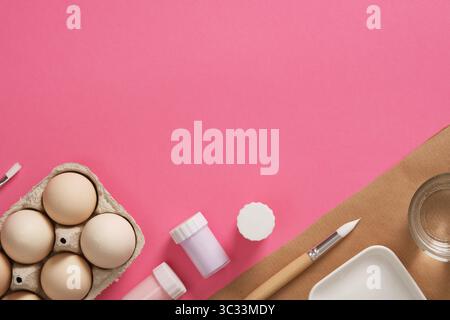 Preparing for the celebration of Easter. Gouache for painting eggs, brushes, palette, glass of water on a pink background. A place for your text. Stock Photo