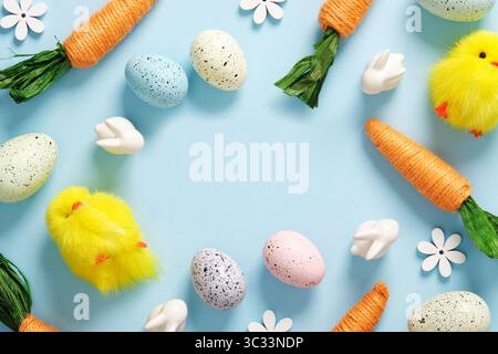 Bright Easter frame with orange carrots, white bunnies, colored eggs and flowers on a blue background. Space for your text. Stock Photo
