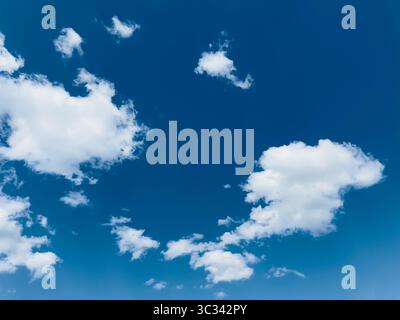 The bright blue sky is filled with beautiful fluffy white clouds on a sunny day. Stock Photo