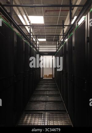 Dark server room corridor featuring metal grid floor and server cabinets, highlighting data center infrastructure Stock Photo