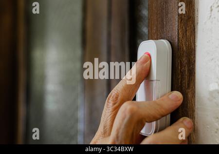 An image of a person's hand pressing a modern doorbell button mounted on a wooden door frame, highlighting the importance of technology and home secur Stock Photo