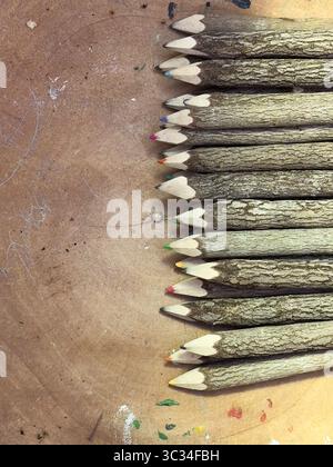 Wooden coloured pencils in a row on a rustic wooden surface. Stock Photo