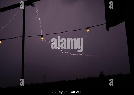 Lightning strike captured over a forested mountain ridge in Trentino, Italy, during a summer thunderstorm. The bolt illuminates the night sky . Stock Photo