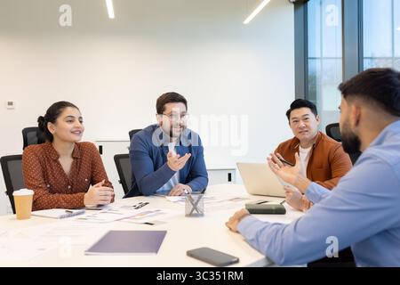 Diverse business team engaged in a meeting, discussing ideas and strategies around a table in a modern office environment. Stock Photo