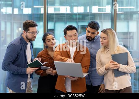 A diverse team collaborates around a laptop in a modern office setting, brainstorming ideas and strategies. Stock Photo