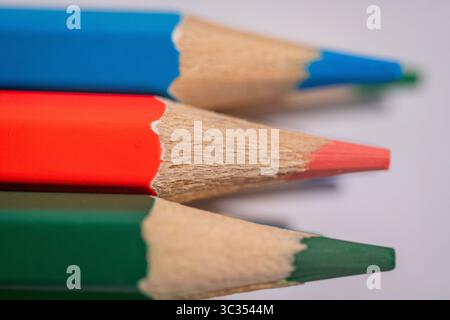 Three pencils with different colors and one of them has a orange tip. The pencils are arranged in a row, with the orange one in the middle Stock Photo