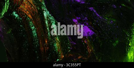 Abstract close-up of wet glass surface with glowing green, orange, and purple neon reflections, featuring fluid streaks and water droplets. Stock Photo