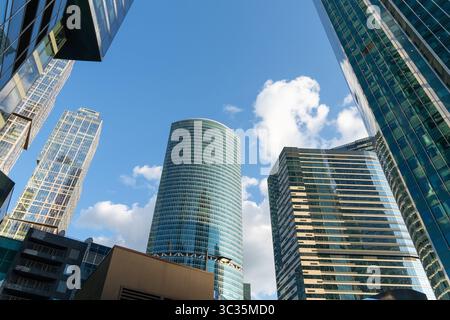 An abstract urban background with skyscrapers featuring mirrored glass facades reflecting fluffy clouds in a bright blue sky, creating a modern and fu Stock Photo