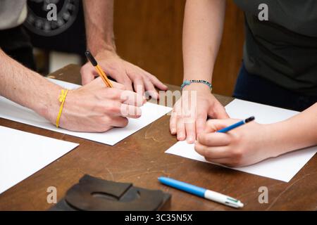 A man and a woman are writing text on a single piece of paper Stock Photo
