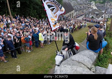 Langholm, UK. 25th July, 2025. Carrying the TownÕs Standard Cornet Ewan Alexander Patterson gallops up the Kirk Wynd during Langholm Common Riding on July 25, 2025 in Langholm, Scotland. A common riding is an equestrian tradition that mainly takes place in the Scottish Borders in Scotland where men and women ride out of the town and along its borders to commemorate the practices from the 13th and 15th centuries when there were frequent raids on the Anglo-Scottish border known as the Border Reivers. In Langholm this event dates back to 1759. ( Credit: Rob Gray/Alamy Live News Stock Photo