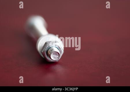 Bolt isolated on dark red background, laying down with nut and washer in front and head is out of focus Stock Photo