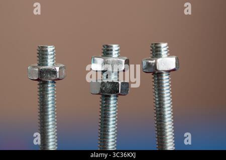Three bolts with nuts isolated on background, middle one has two nuts and others one Stock Photo
