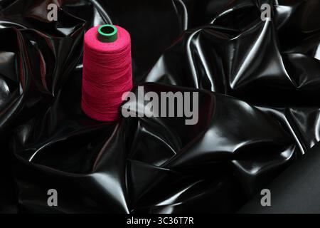 Glossy, black patent artificial leather with pink sewing thread atop. The sleek, reflective surface contrasts with the texture of sewing thread. Stock Photo