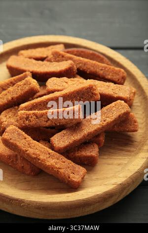 Tasty rye croutons on wooden plate on black background. Top view Stock Photo