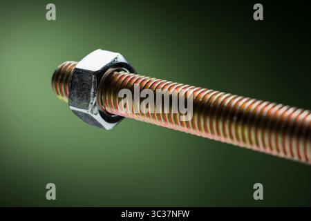 Close-up of large steel screw with bolt on green background. Stock Photo