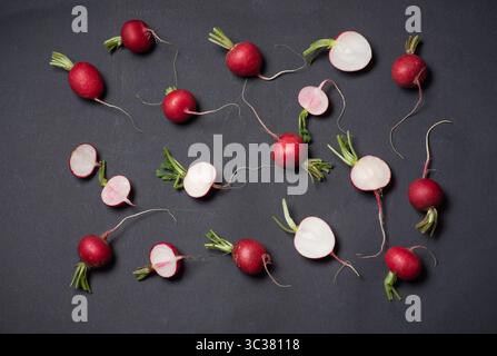An artistic arrangement of scattered fresh radishes alongside sliced halves on a dark surface showcases the vibrant colors and textures, celebrating t Stock Photo