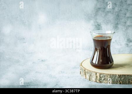 Scandinavian minimalism: single glass of rich filter coffee resting on raw wood slice against textured pale-grey wall, generous negative space suggest Stock Photo