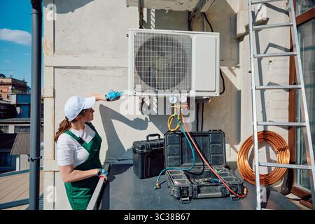 Technician inspecting air conditioning unit on building rooftop under clear blue sky Stock Photo